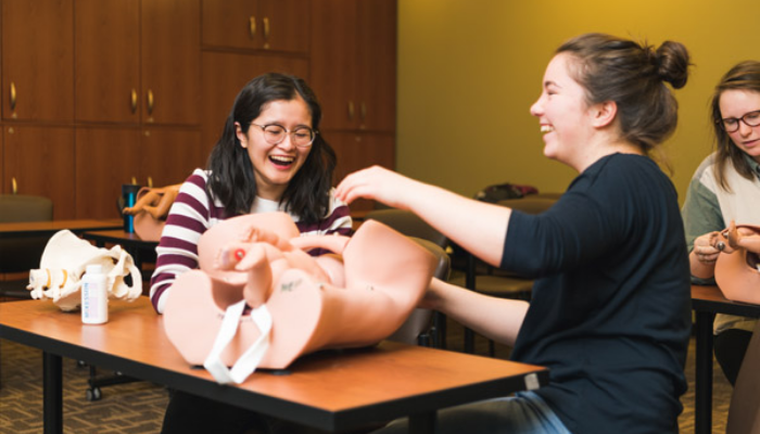 Two midwifery students sit at a desk while engaging in simulation-based learning.