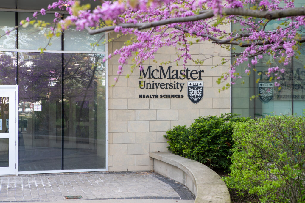 The entrance to McMaster University’s Health Sciences Centre with trees and bushes in the nearby garden.