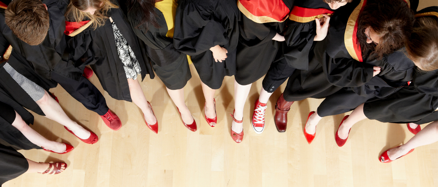 A group of midwifery graduates stand with a foot forward showing off their red shoes.